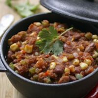 Overhead view of classic vegan chili with beans, corn, and cilantro in a black cast iron pot