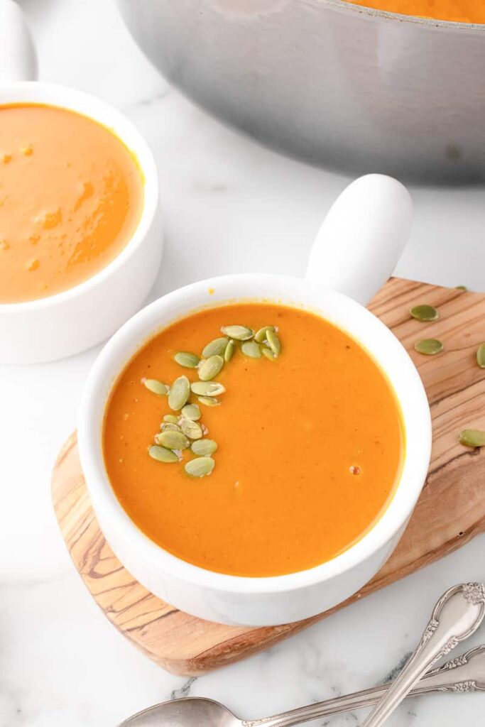 Bowl of coconut curry pumpkin soup topped with pepitas on a wooden board