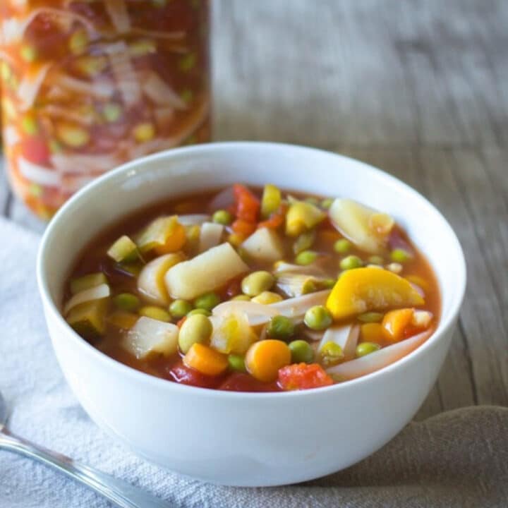 Edamame vegetable soup with zucchini, carrots, potatoes, and peas in a white bowl