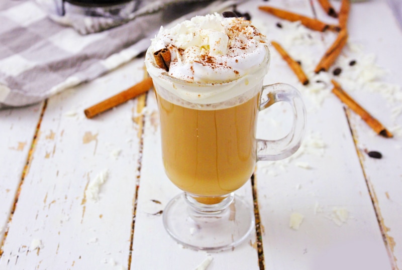 Glass mug of vegan pumpkin spice latte surrounded by cinnamon sticks