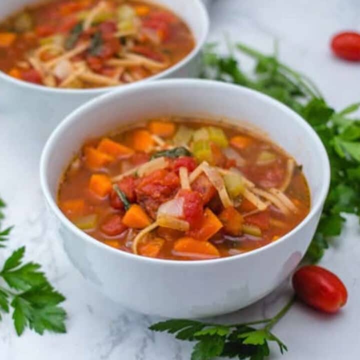 Italian minestrone noodle soup with carrots, tomatoes, and broken fettuccine in a white bowl