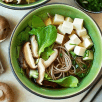 Japanese soba noodle soup with cubed tofu, shiitake mushrooms and baby bok choy in a green bowl