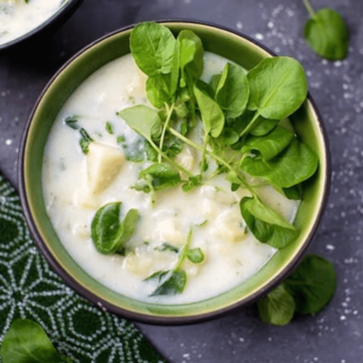 Bowl of creamy leek and potato soup topped with fresh watercress leaves