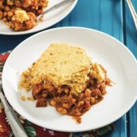 Plated serving of vegan maple baked beans and cornbread casserole with a second plate in the background