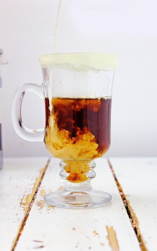 Pouring almond milk into spiced pumpkin coffee in a glass mug