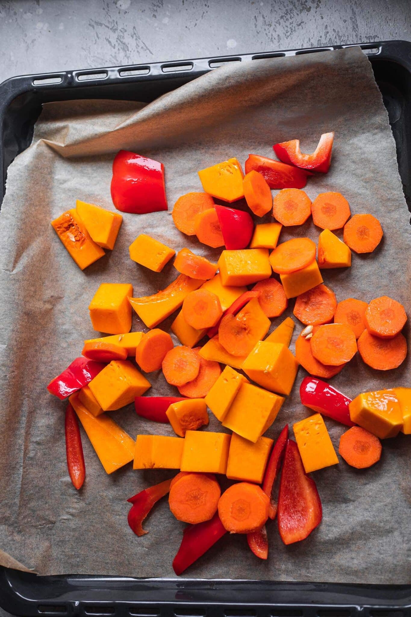 Cubed pumpkin, sliced carrots and red pepper on a parchment-lined baking tray before roasting