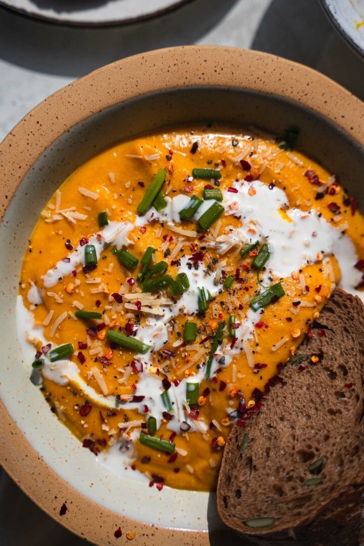 Roasted vegetable pumpkin soup garnished with coconut cream, fresh chives and chili flakes