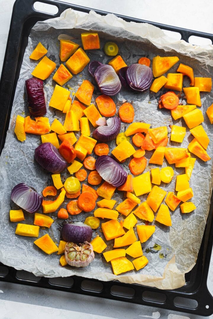 Roasted pumpkin, carrots, red onion and a whole garlic bulb on a baking tray