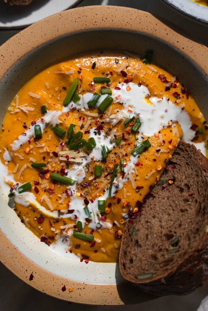 Two bowls of roasted vegetable pumpkin soup with slices of bread on the side