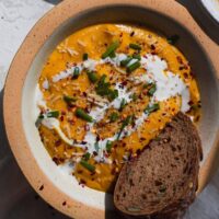 Roasted vegetable pumpkin soup in a speckled bowl with coconut cream swirl and rye bread