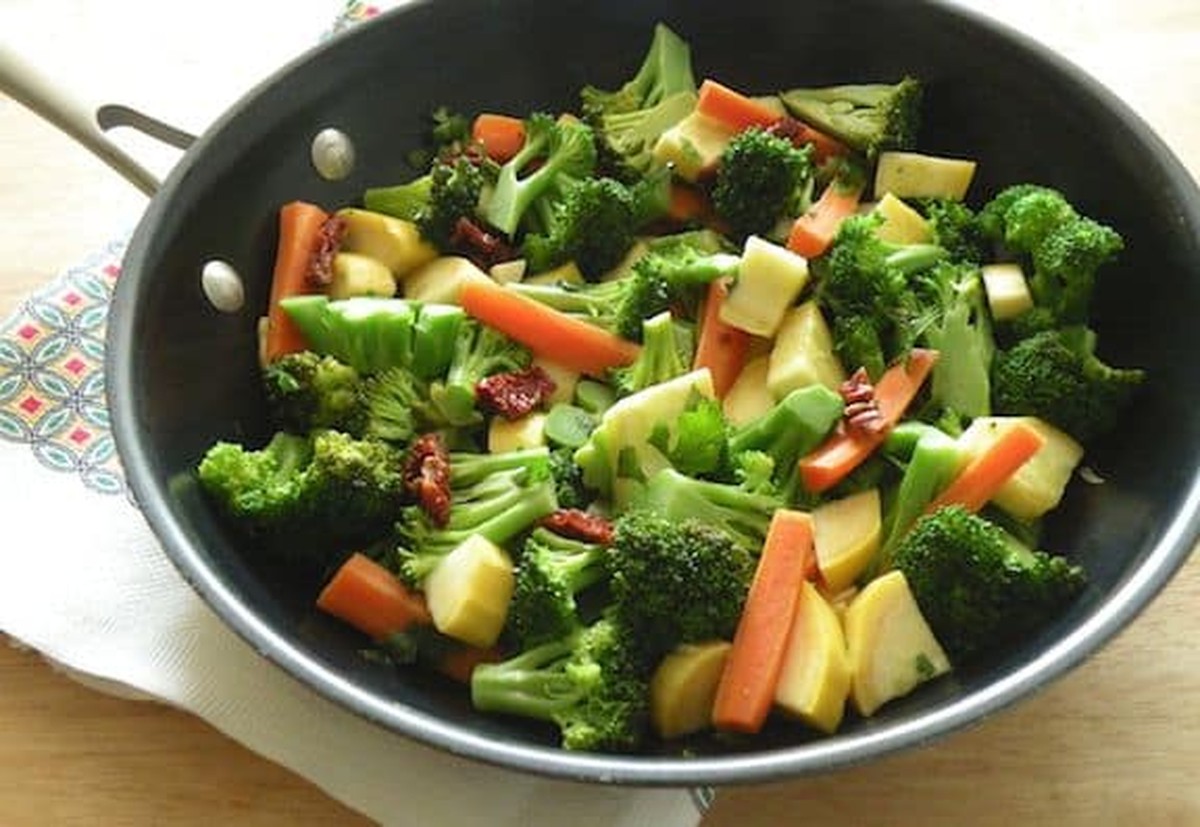 A wide skillet full of sautéed broccoli, carrots, yellow squash, and sun-dried tomatoes
