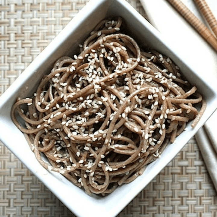 Vegan sesame soba noodles topped with sesame seeds in a white bowl