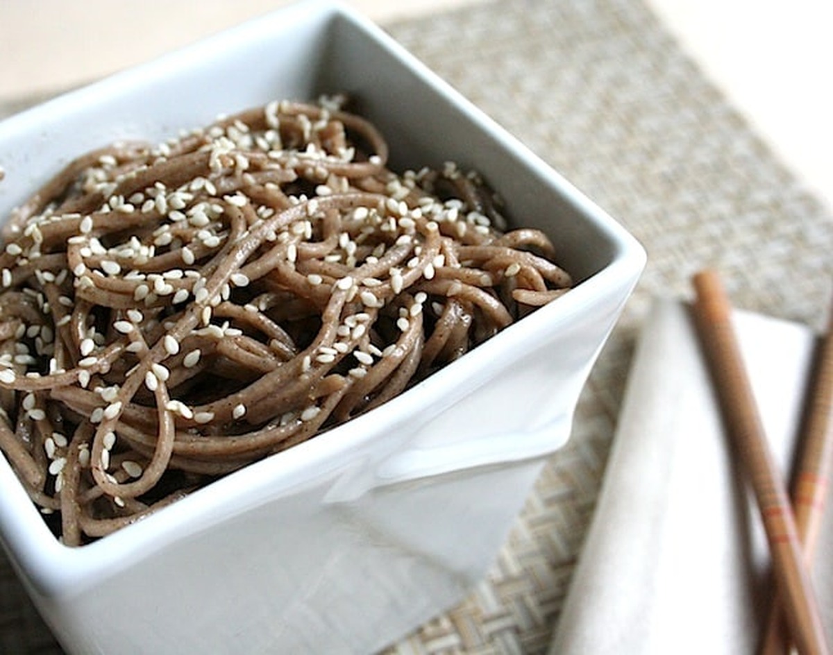 Sesame soba noodles topped with toasted sesame seeds in a square white bowl