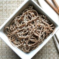 Overhead view of vegan sesame soba noodles in a white bowl with chopsticks