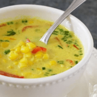 Thai coconut corn soup with red bell pepper and scallions in a white bowl with a spoon