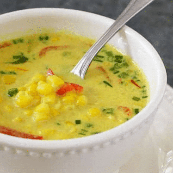 Thai coconut corn soup with red bell pepper and scallions in a white bowl with a spoon