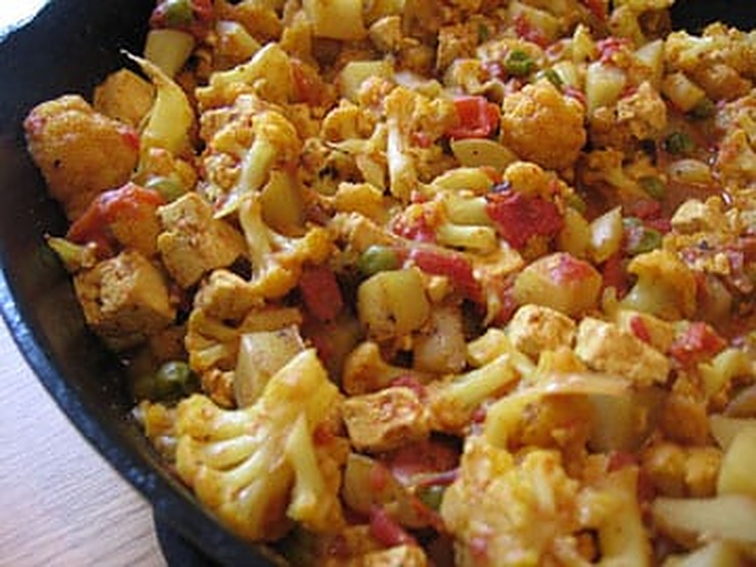 Tofu aloo gobi with cauliflower, potatoes, tofu, tomatoes and peas in a cast-iron skillet