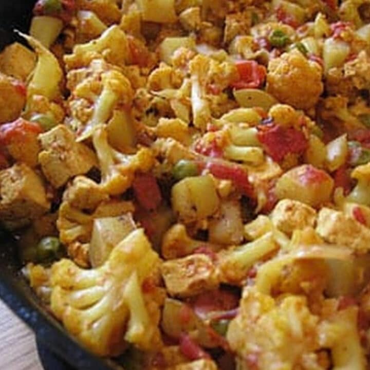 Tofu aloo gobi with cauliflower, potatoes, tofu and peas in a cast-iron skillet