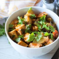 Tofu and vegetable stew in a white bowl topped with fresh cilantro