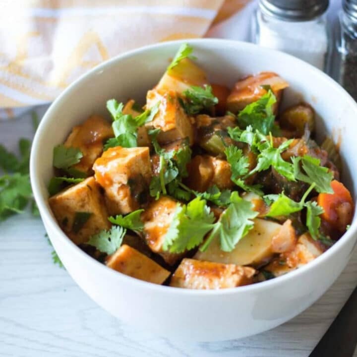Tofu and vegetable stew in a white bowl topped with fresh cilantro