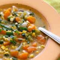 Overhead close-up of vegan butternut squash, sweet potato, and corn chowder in a terracotta bowl, garnished with scallions