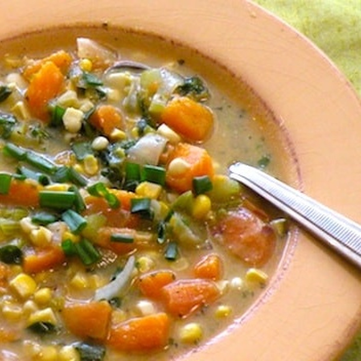 Overhead close-up of vegan butternut squash, sweet potato, and corn chowder in a terracotta bowl, garnished with scallions