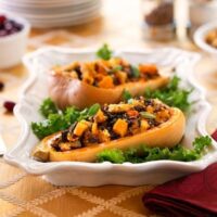 Vegan butternut squash halves stuffed with wild rice, whole wheat bread, and onions, garnished with sage and kale