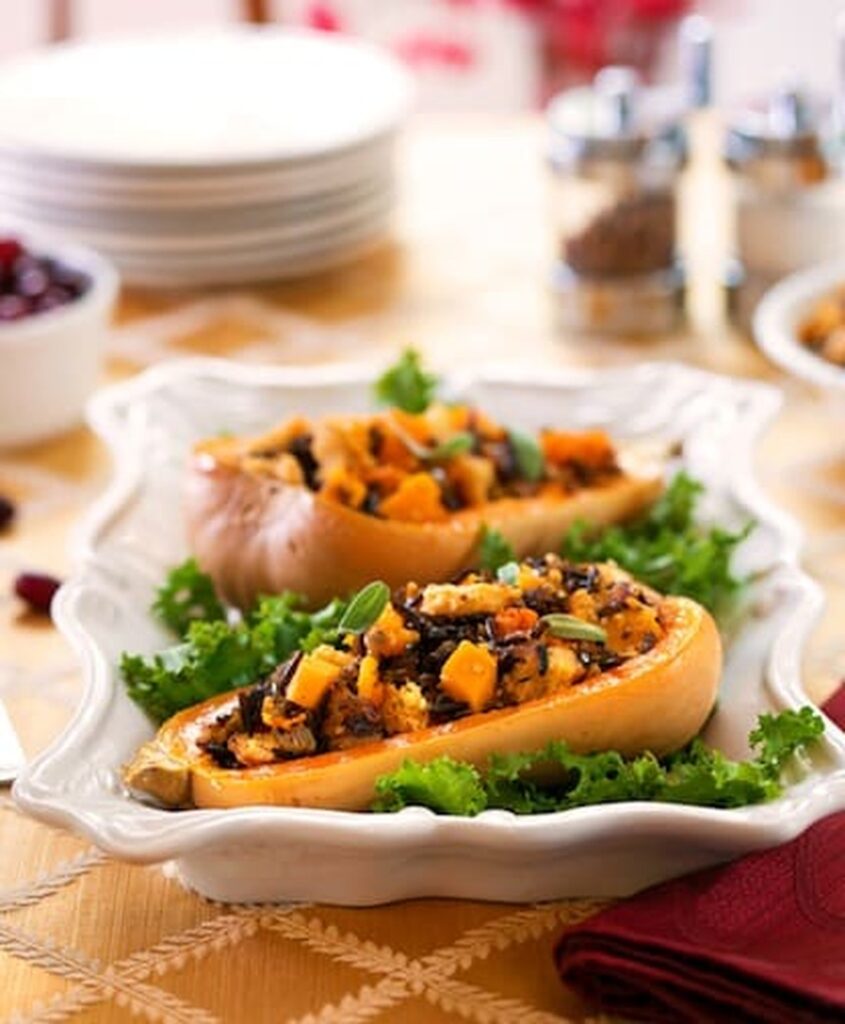 Vertical photo of vegan stuffed butternut squash with wild rice and onion stuffing on a white platter with kale