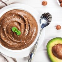 Vegan avocado chocolate maca mousse in a bowl with avocado and hazelnuts