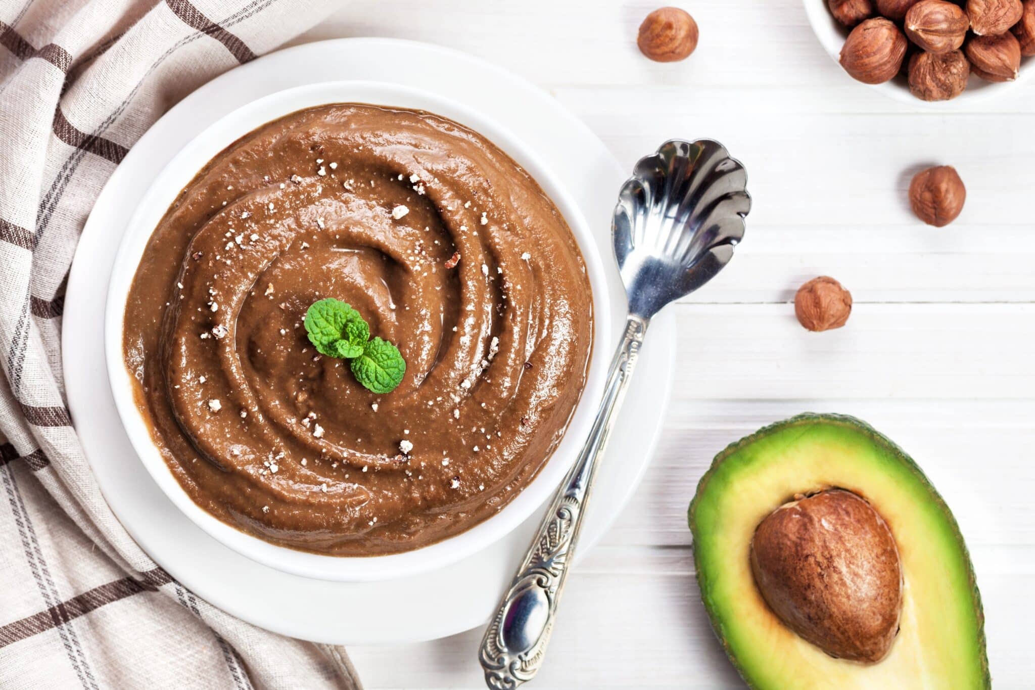Vegan avocado chocolate maca mousse in a bowl with avocado and hazelnuts
