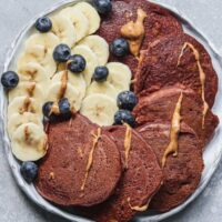 Overhead view of chocolate pumpkin pancakes with banana slices, blueberries and nut butter on a white plate