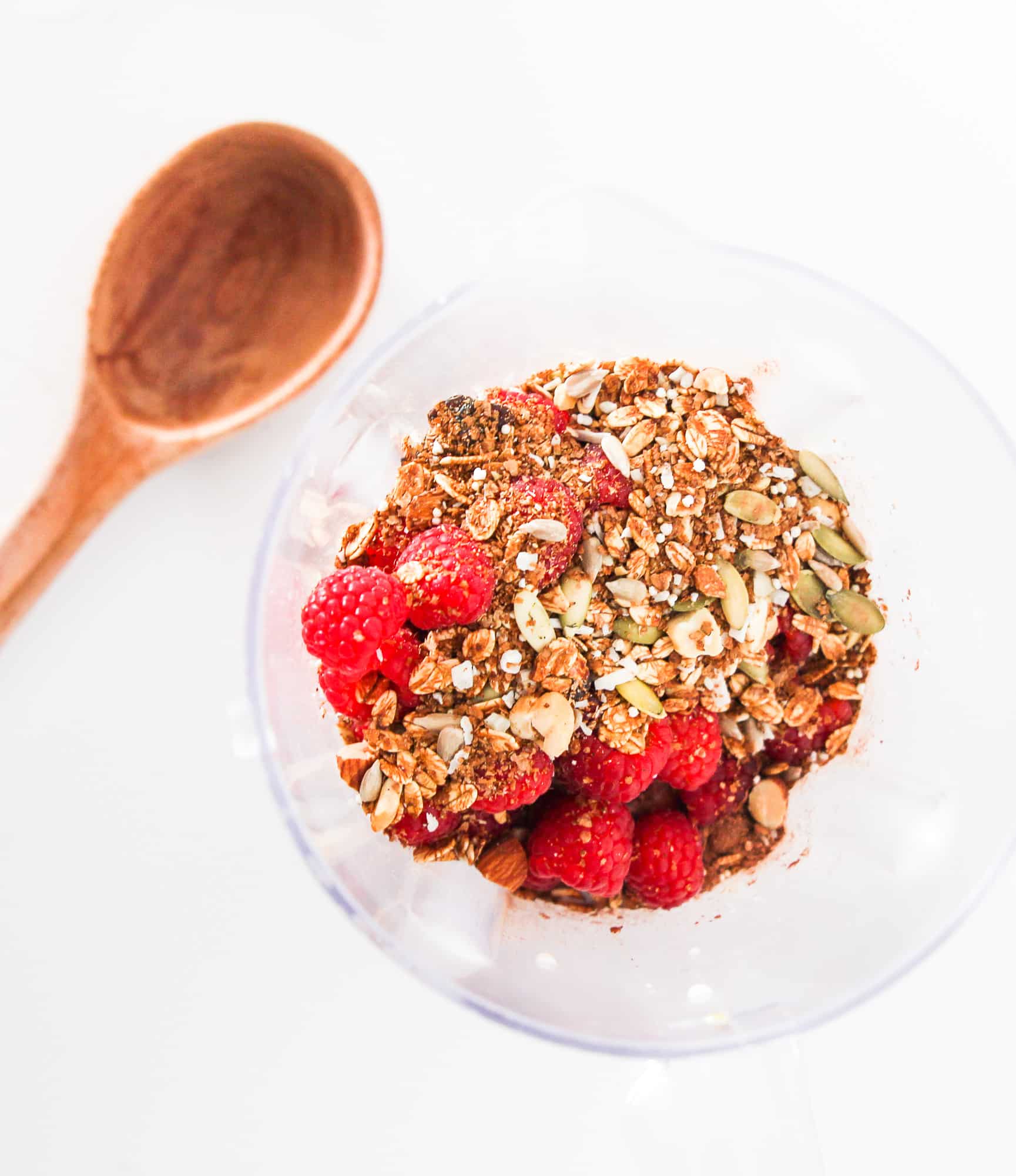 Frozen raspberries, granola, and cacao powder in a blender before blending into a chocolate raspberry smoothie