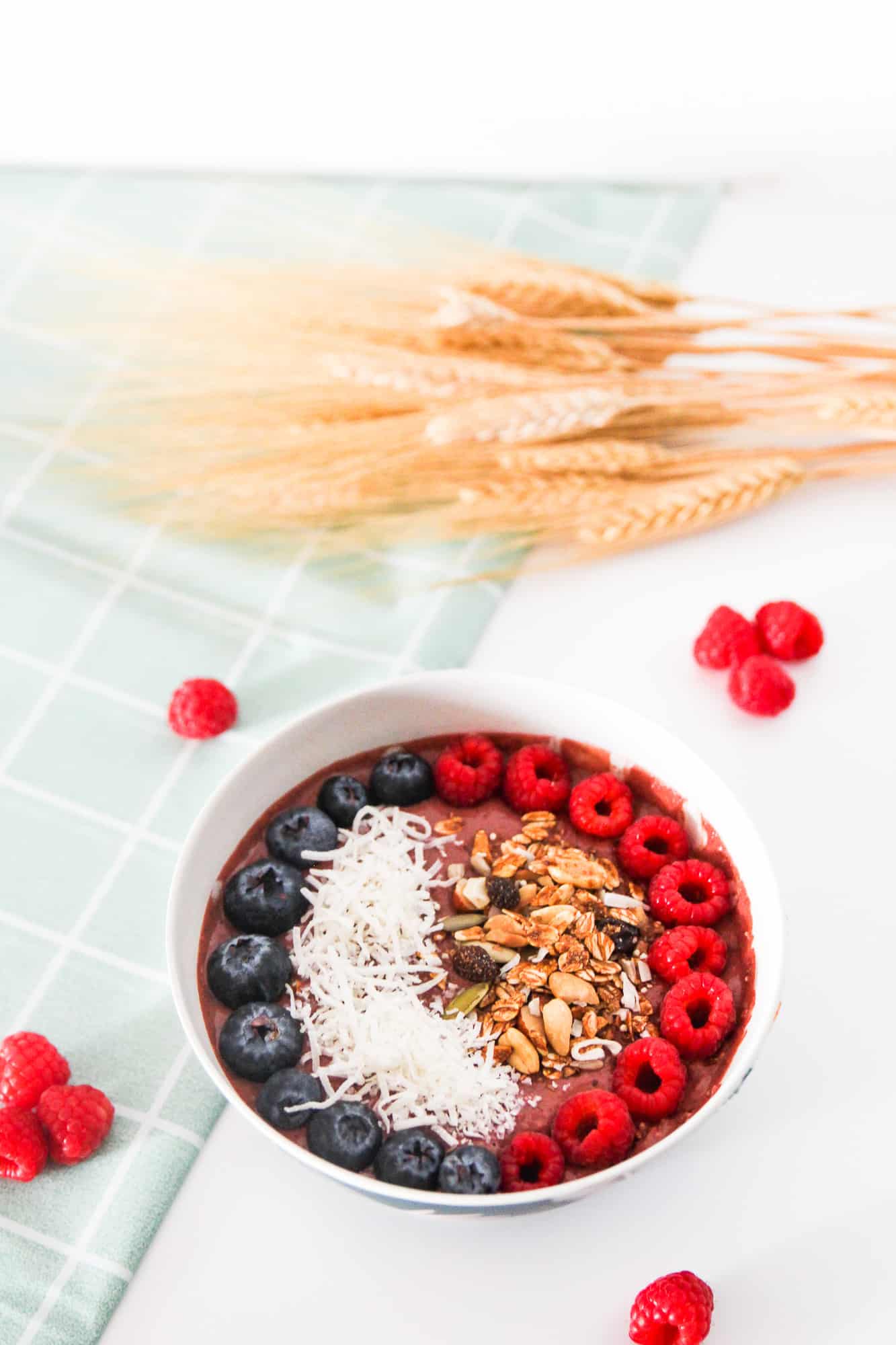 Vegan chocolate raspberry smoothie bowl garnished with fresh berries and shredded coconut, styled with dried wheat stalks