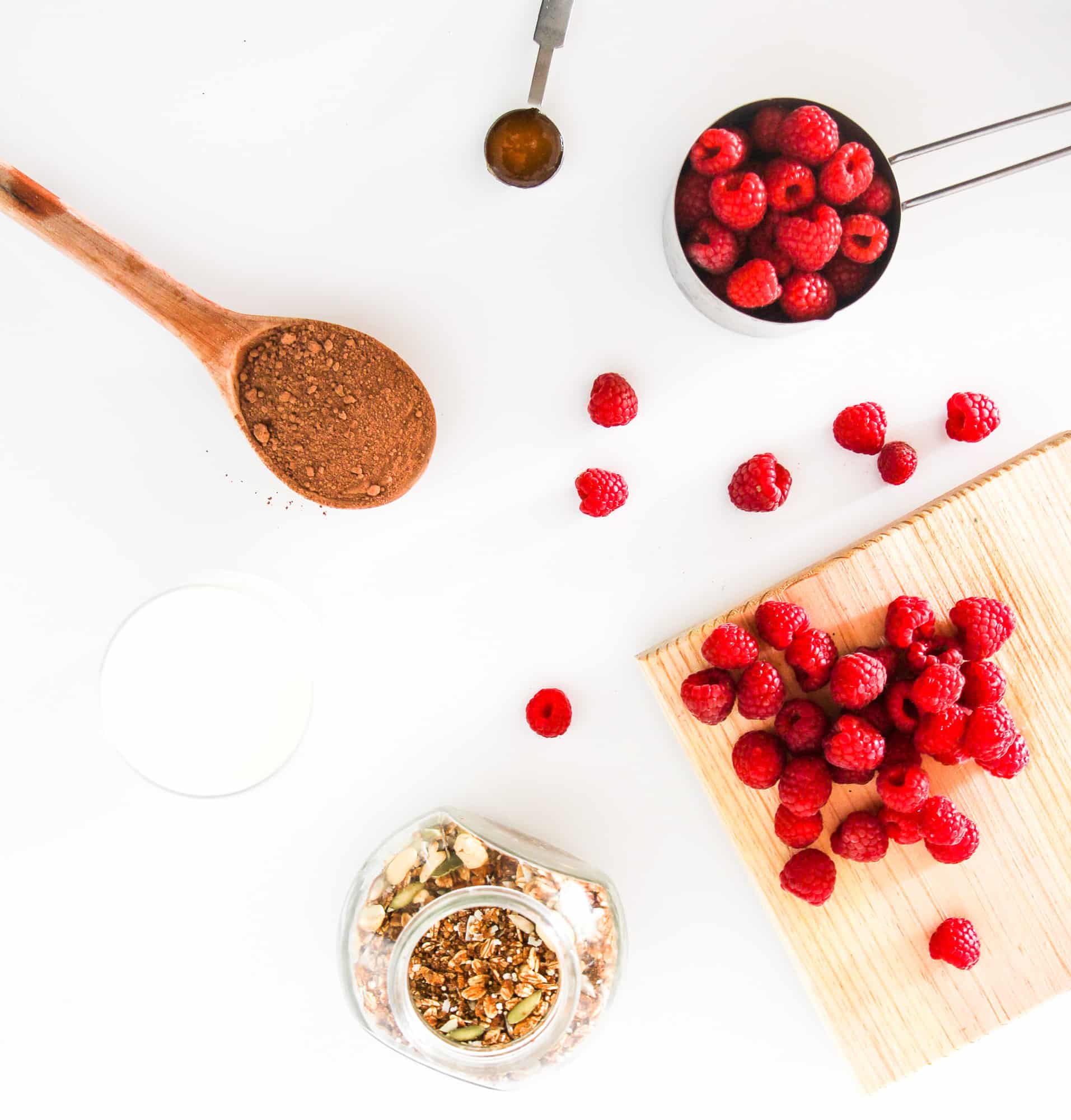 Ingredients for a vegan chocolate raspberry smoothie bowl, including frozen raspberries, cacao powder, granola, and plant-based milk