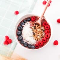 Overhead view of a vegan chocolate raspberry smoothie bowl topped with fresh raspberries, blueberries, shredded coconut, and granola