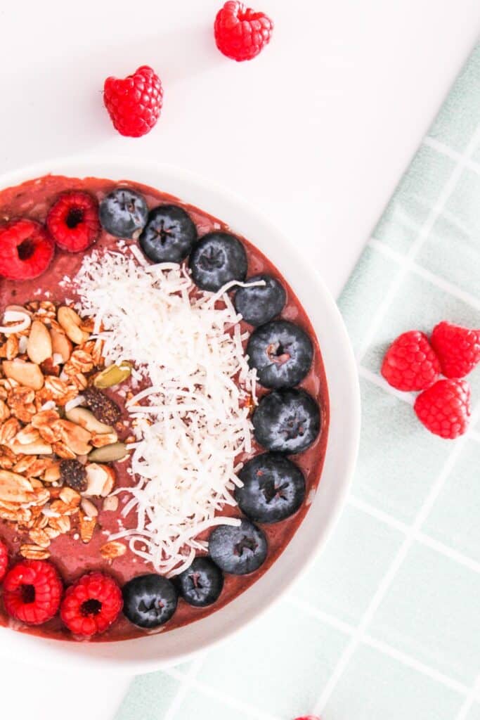 Vegan chocolate raspberry smoothie bowl topped with berries, coconut, and granola on a light marble surface