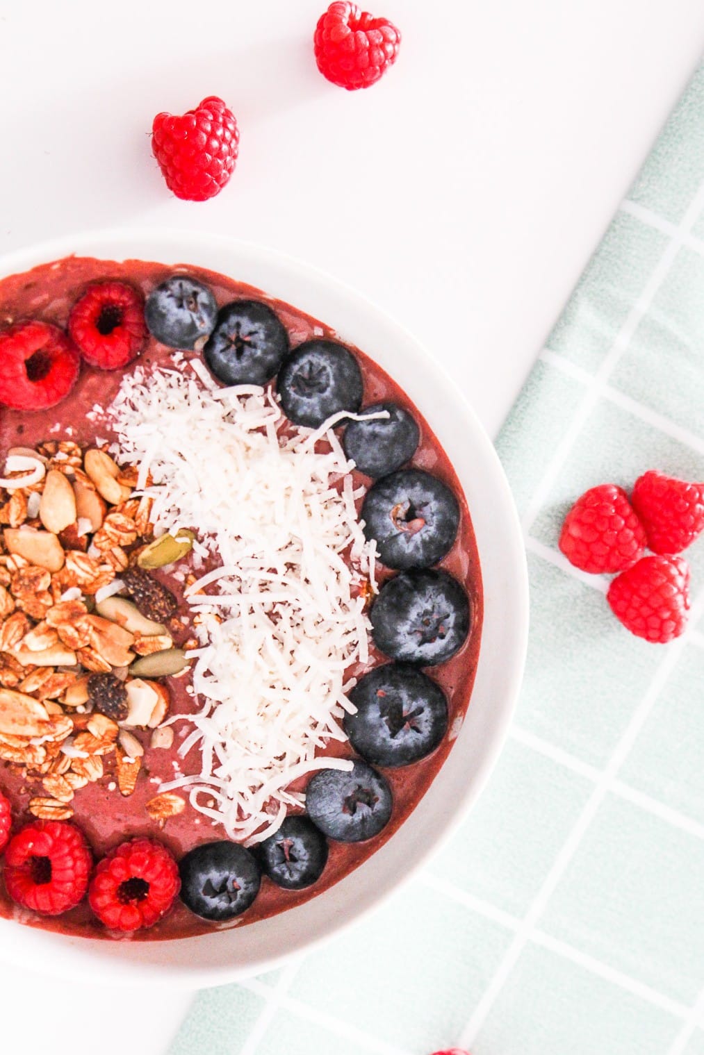Vegan chocolate raspberry smoothie bowl topped with berries, coconut, and granola on a light marble surface