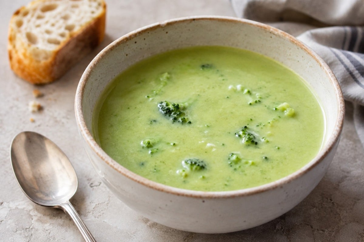 Vegan cream of broccoli soup in a bowl with bread and a spoon