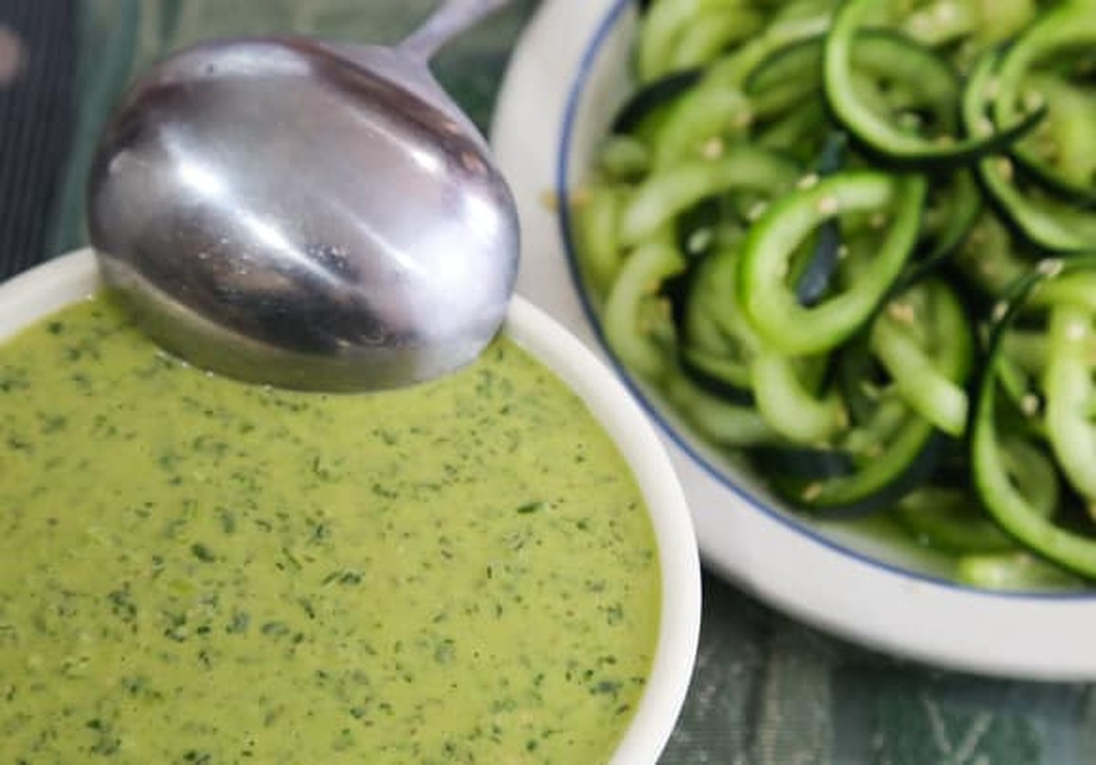 Vegan green goddess dressing in a white bowl next to a bowl of spiralized cucumber noodles