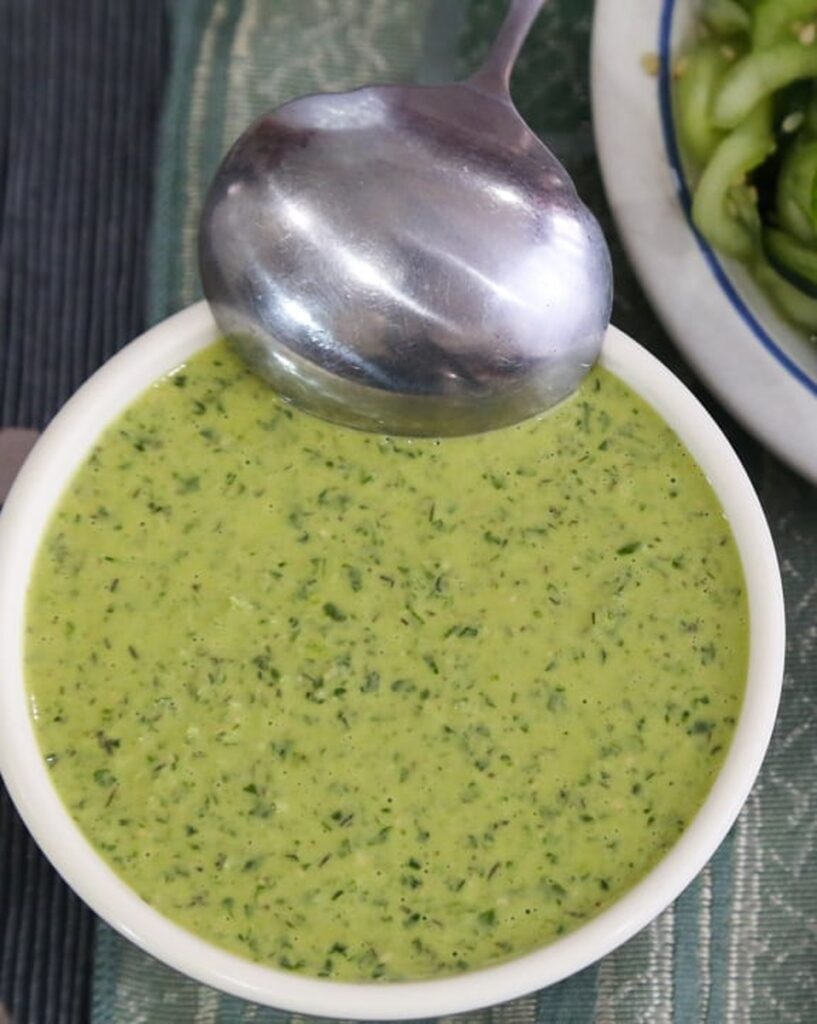 Close-up of creamy vegan green goddess dressing in a white bowl with a metal spoon