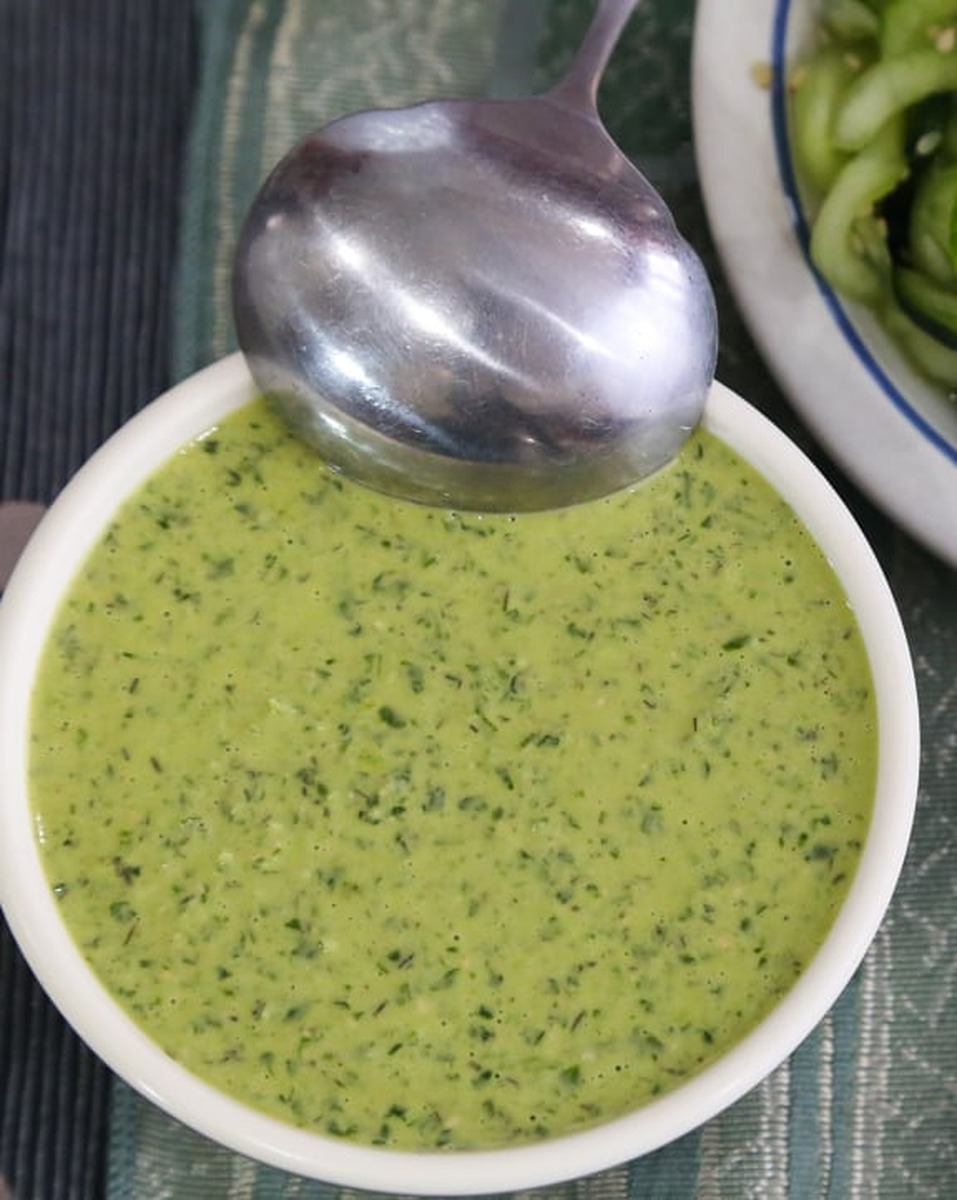 Close-up of creamy vegan green goddess dressing in a white bowl with a metal spoon
