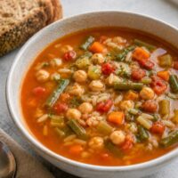 Vegan orzo minestrone soup with chickpeas and vegetables in a white bowl