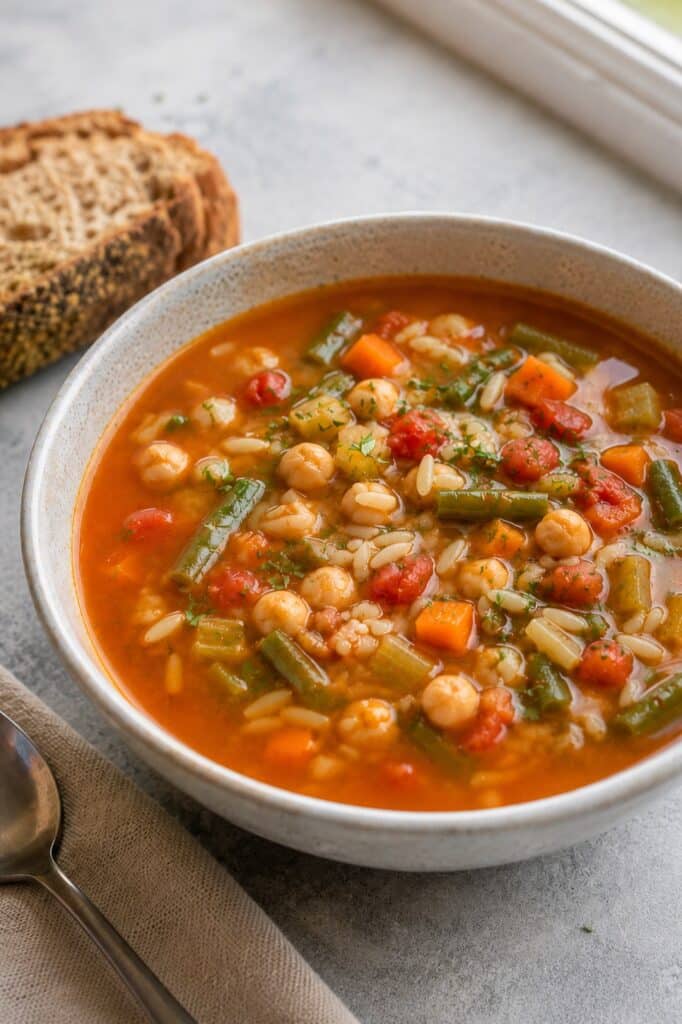 Vegan orzo minestrone soup with chickpeas, green beans, and carrots in a white bowl