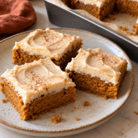 Frosted vegan pumpkin bars dusted with cinnamon on a stoneware plate