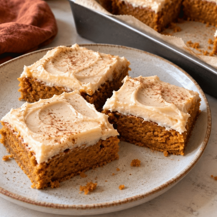 Frosted vegan pumpkin bars dusted with cinnamon on a stoneware plate