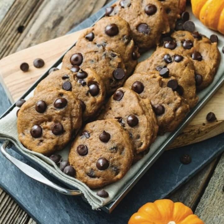 Vegan pumpkin chocolate chip cookies on a metal serving tray with mini pumpkins