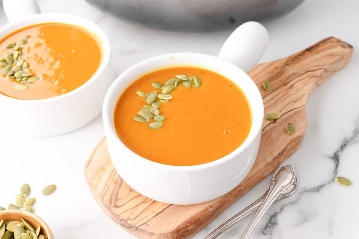 Two bowls of vegan pumpkin curry soup with pepitas on a marble counter