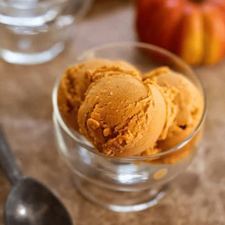 Scoops of vegan pumpkin ice cream in a glass dish with a small pumpkin in the background