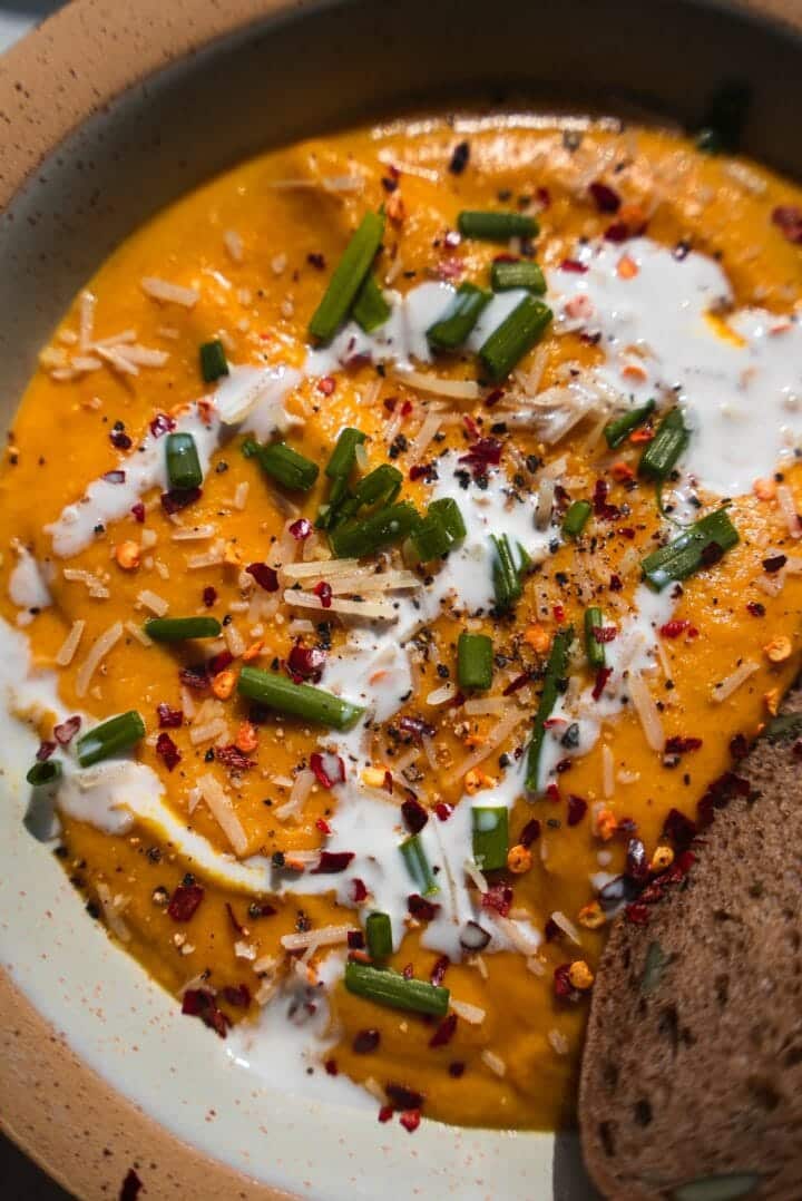 Close-up of vegan pumpkin soup with coconut cream, chives and a slice of bread