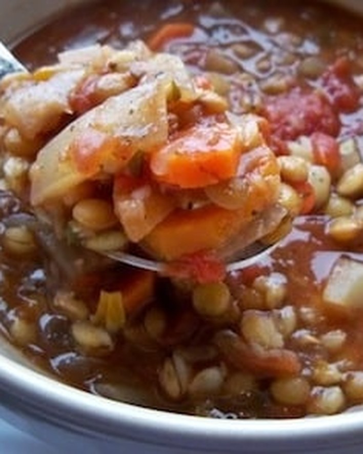 Spoonful of vegan tomato lentil soup with barley, carrots, and cabbage lifted from the bowl